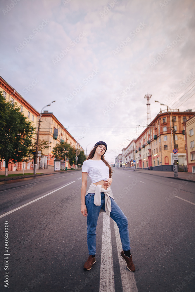 Girl posing in the middle of the roadway. Girl in stylish clothes and hat.