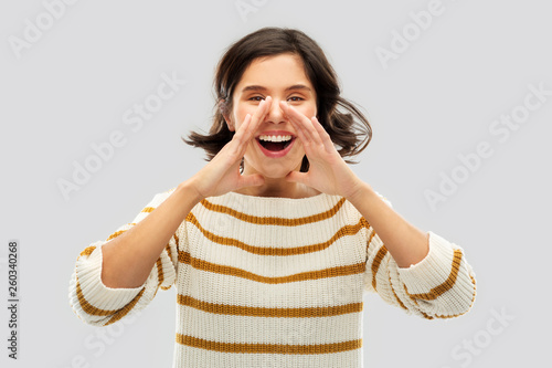 people concept - happy smiling young woman in striped pullover calling someone over grey background