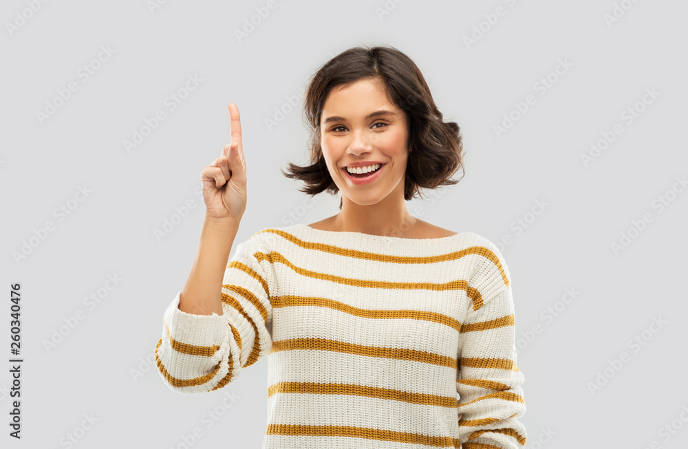 gesture, counting and people concept - happy smiling young woman in striped pullover showing one finger or pointing up over grey background gesture, counting and people concept - happy smiling young woman in striped pullover showing one finger or pointing up over grey background