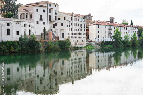 white houses along river Brenta in Bassano del Grappa, Italy. With reflection in water