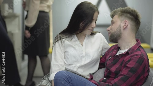 Pretty shy lady sitting near attractive bearded man in casual closing in the modern office. The guy kissing his girlfriend in the cheek, she is smiling. Flirting and love affair at work photo