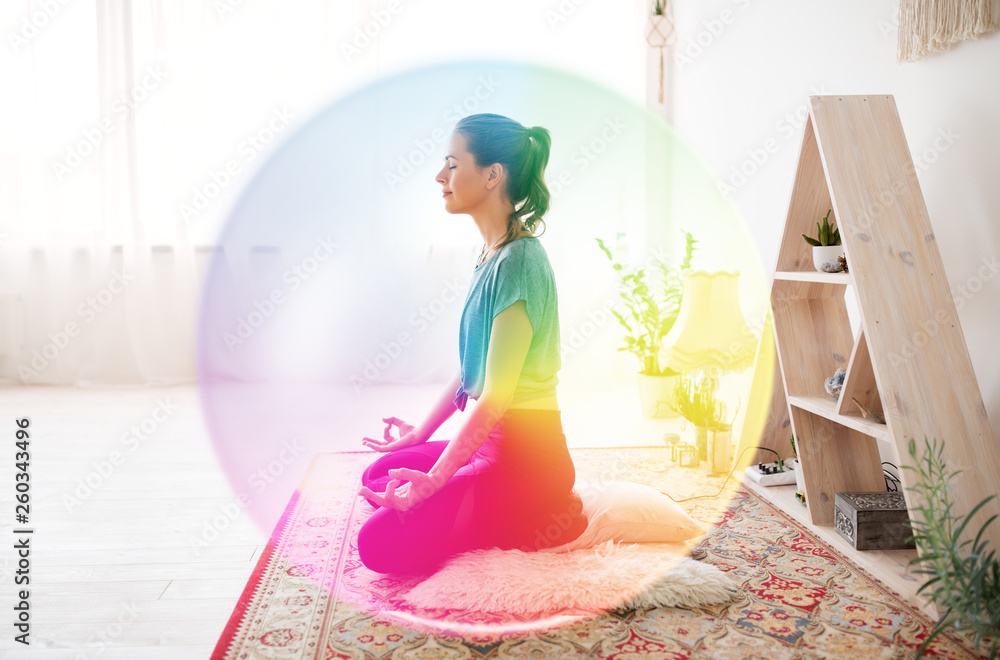 mindfulness, spirituality and healthy lifestyle concept - woman meditating in lotus pose at yoga studio over rainbow aura - obrazy, fototapety, plakaty 