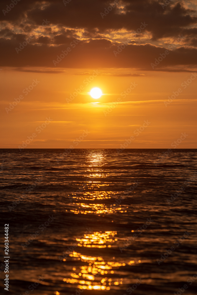 colorful sunset over calm sea beach with dark blue water and dramatic contrasty clouds