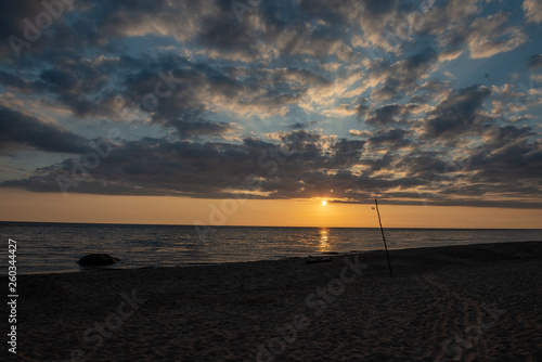 colorful sunset over calm sea beach with dark blue water and dramatic contrasty clouds