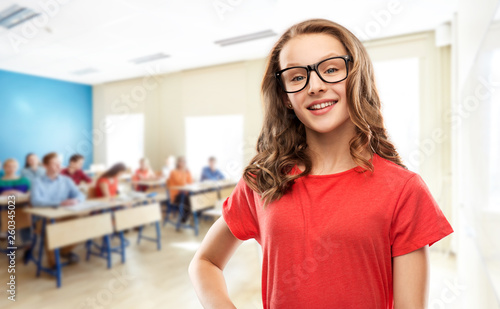 education, school and people concept - smiling teenage student girl in glasses and red t-shirt over classroom background