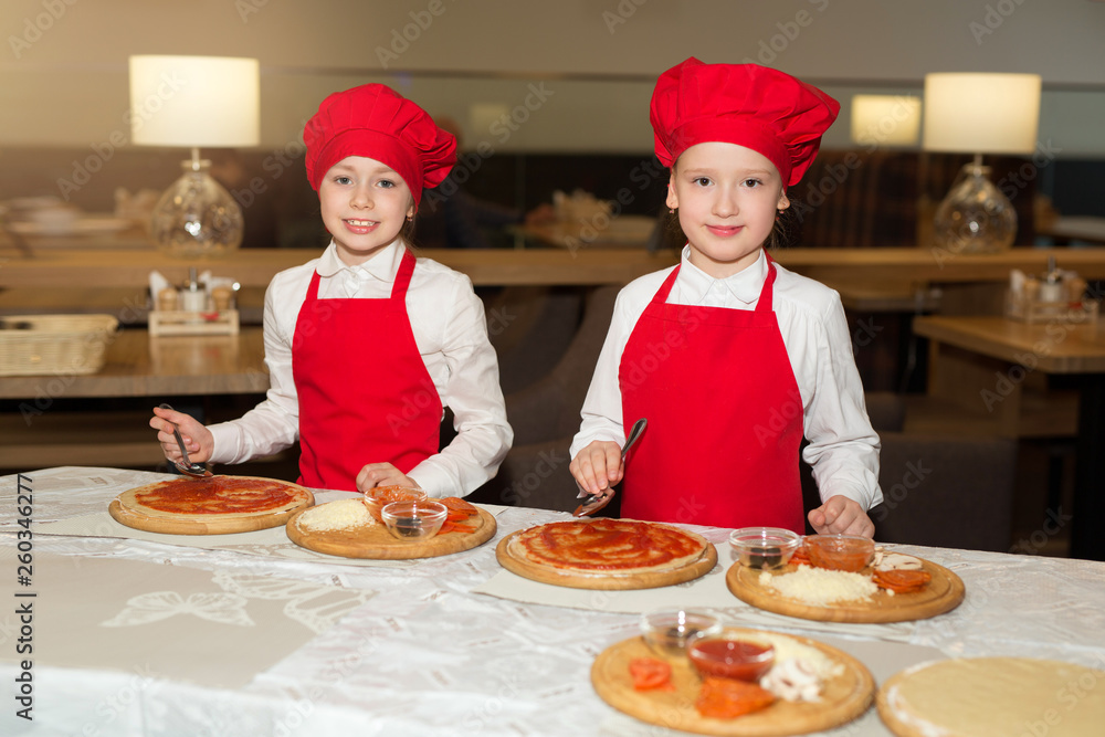 two beautiful cook girls in white shirts and red aprons in the restaurant make pizza two beautiful cook girls in white shirts and red aprons in the restaurant make pizza