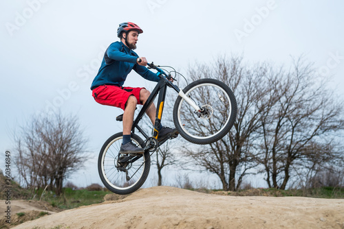 Young cyclist in a blue sweater and red shorts riding over the dirt.
