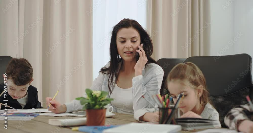 In a modern house businesswoman and mature mother speaking on phone while doing home with her three children , on the sofa background grandmother reading a book. In a modern house businesswoman and mature mother speaking on phone while doing home with her three children , on the sofa background grandmother reading a book.