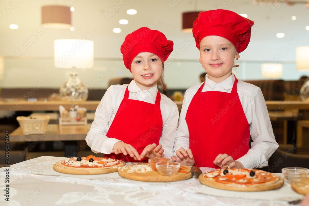 two beautiful cook girls in white shirts and red aprons in the restaurant make pizza two beautiful cook girls in white shirts and red aprons in the restaurant make pizza