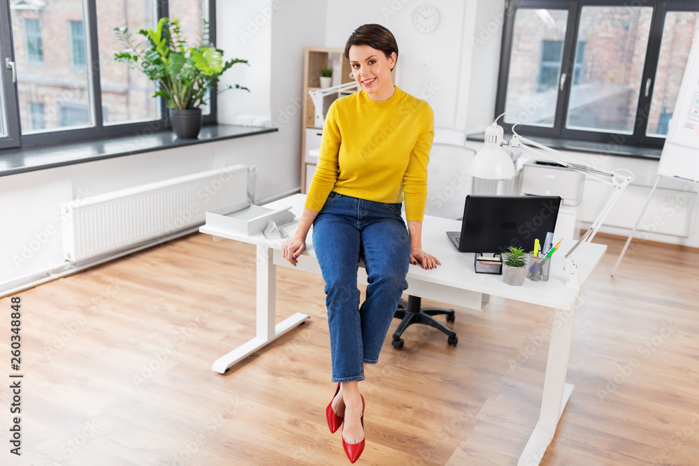 business and people concept - happy businesswoman sitting on desk at office business and people concept - happy businesswoman sitting on desk at office