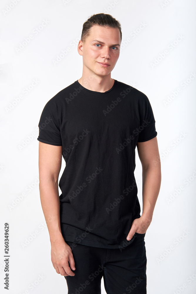 Obraz premium Handsome young smiling man wearing a black cotton short-sleeved T-shirt and black jeans posing in studio.