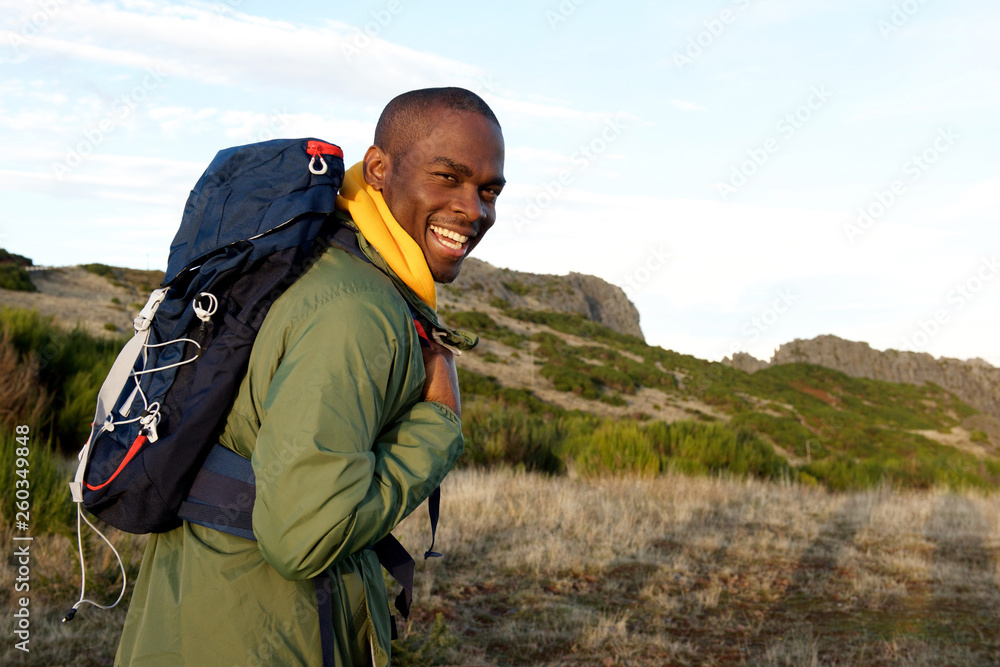 happy african american man hiking with backpack in the mountains