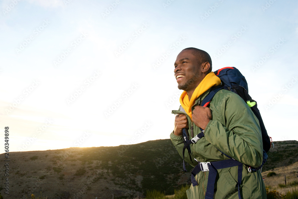 Side of happy african american man hiking in nature with backpack