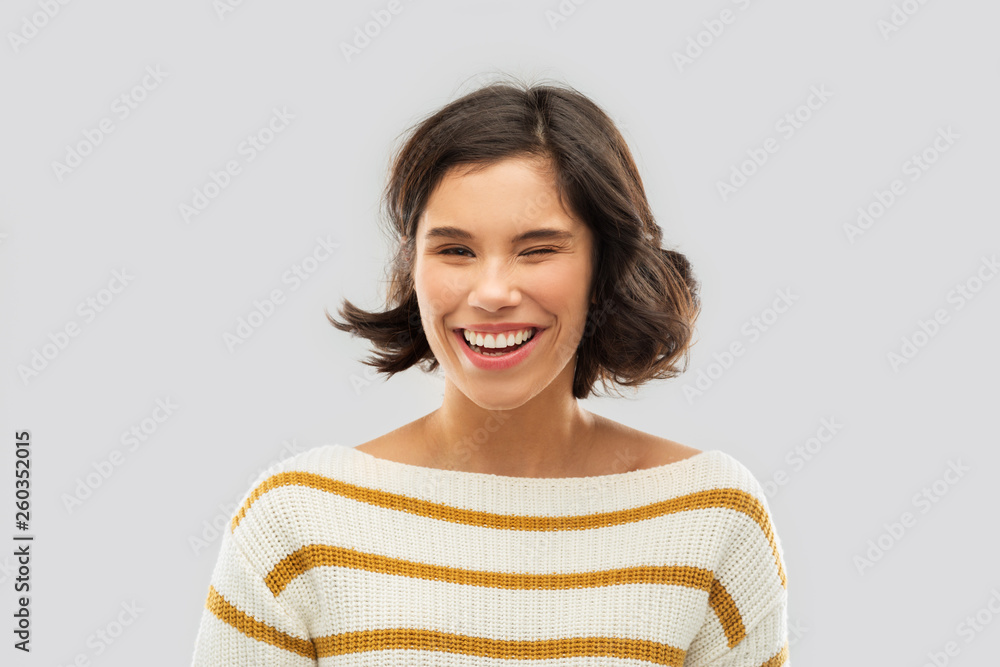 expression and people concept - happy smiling young woman in striped pullover winking over grey background expression and people concept - happy smiling young woman in striped pullover winking over grey background