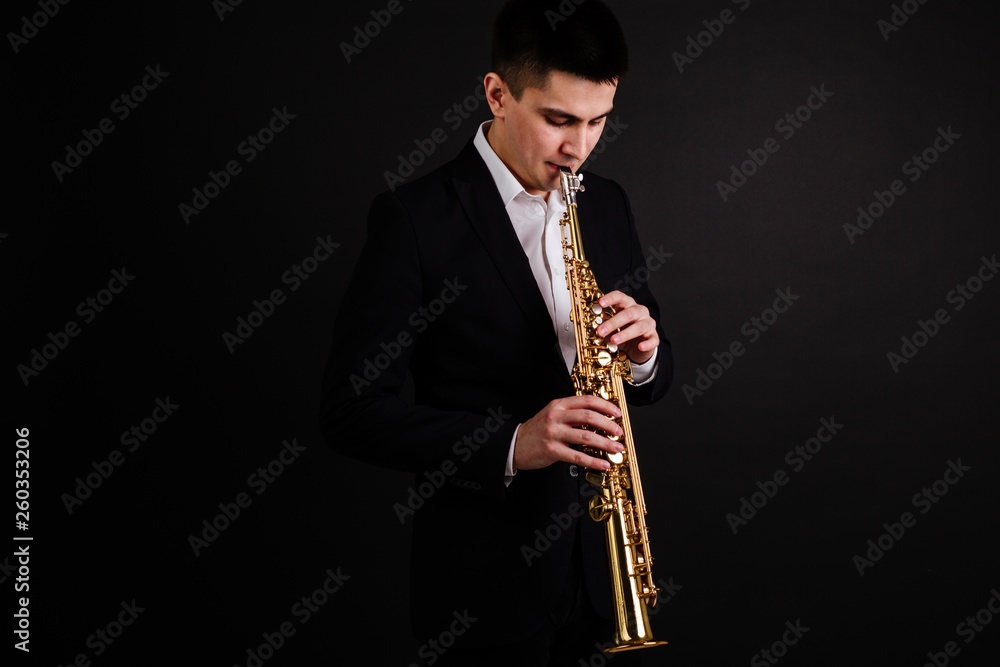 Naklejka premium Saxophonist in black classic suit playing jazz on soprano saxophone