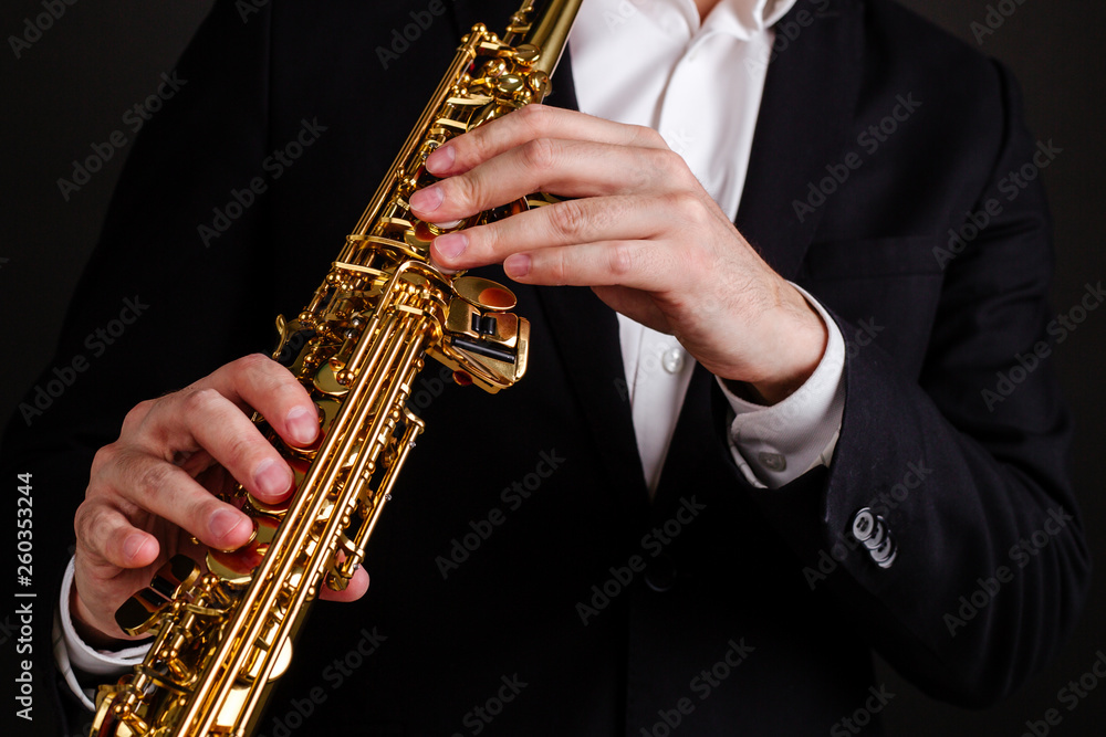 Fototapeta premium Saxophonist in black classic suit playing soprano saxophone in jazz orchestra close-up