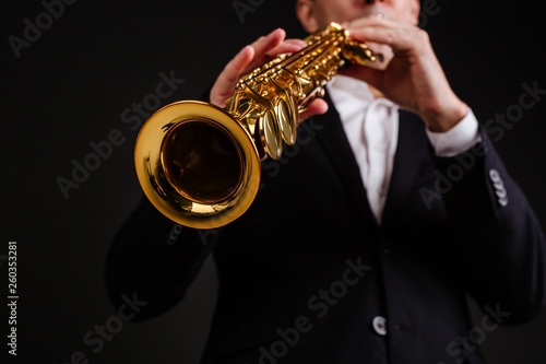 Saxophonist in a black classic suit playing the soprano saxophone close-up