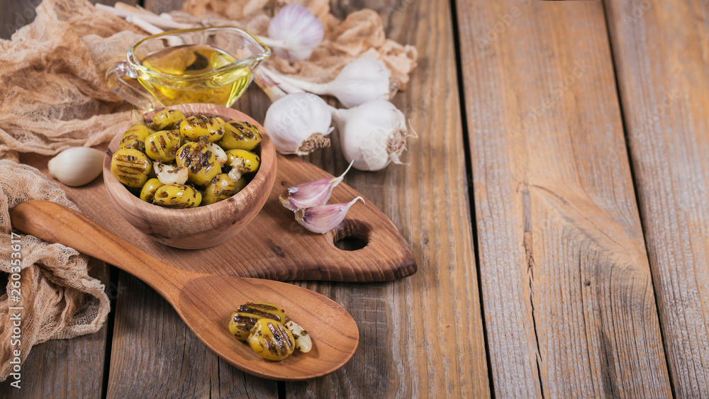 Grilled olives with garlic, olive oil and spices on wooden background Grilled olives with garlic, olive oil and spices on wooden background