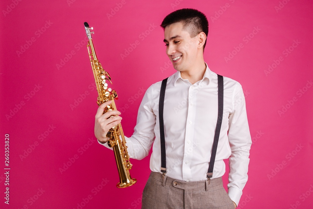 Naklejka premium Saxophonist holding a saxophone in his hand on a pink background