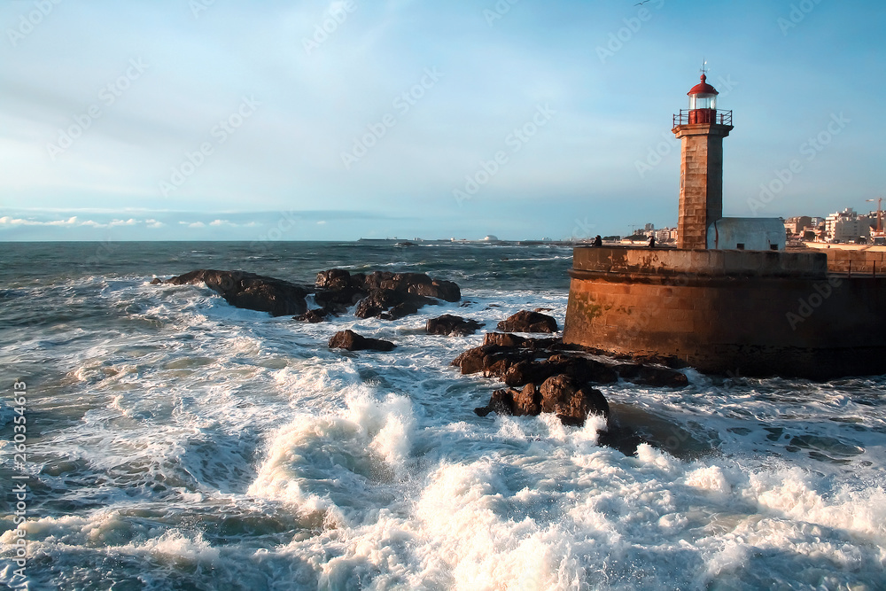 The waves of the Atlantic Ocean crash against the rocks at sunset by the lighthouse