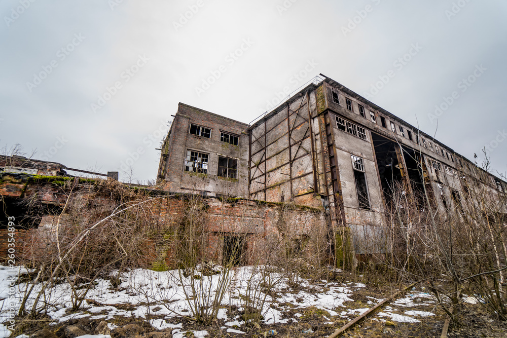 Ruined factory or abandoned warehouse hall with broken windows and doors outside in winter. Remains of the destroyed industrial buildings on the snowy background.