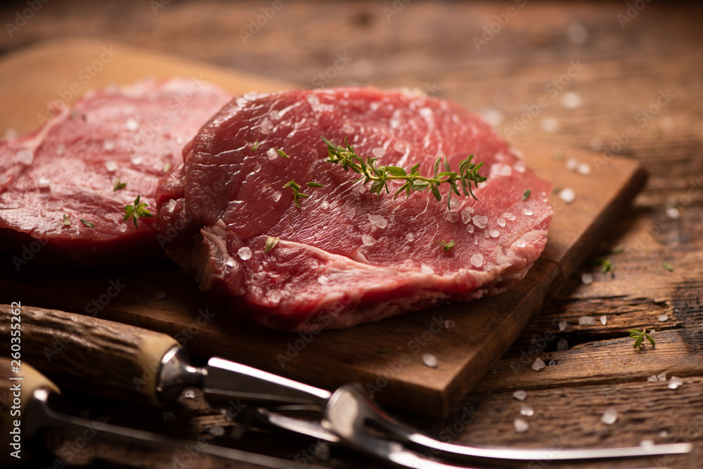 Raw beef steak and spices on wooden cutting board Raw beef steak and spices on wooden cutting board