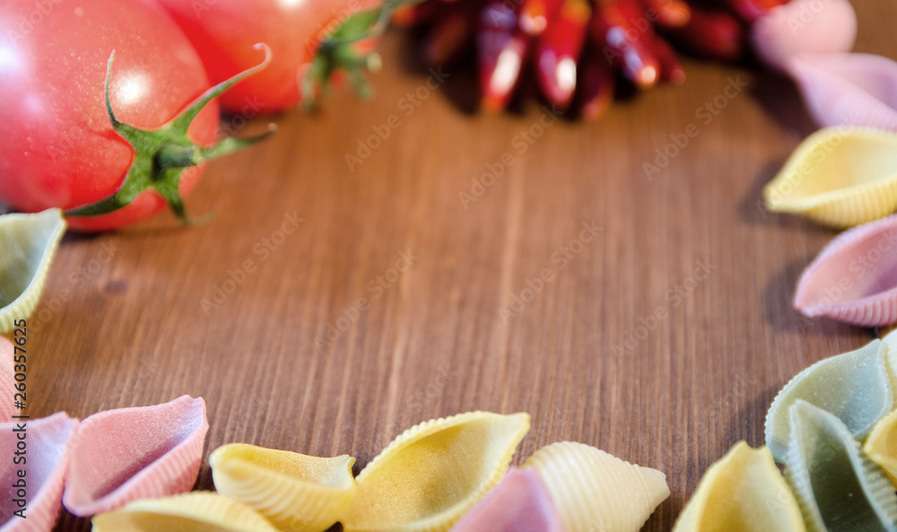 Still life of uncooked colored pasta with bunch of red dry pepper and red tomatoes Still life of uncooked colored pasta with bunch of red dry pepper and red tomatoes