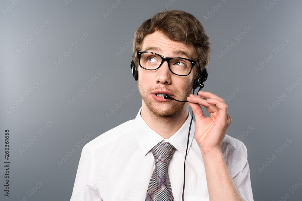 dreamy call center operator in headset and glasses looking away on grey background dreamy call center operator in headset and glasses looking away on grey background