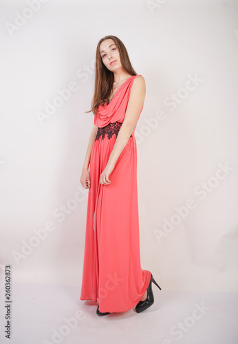 charming young girl in red evening long dress with black lace stands on a white background in the Studio