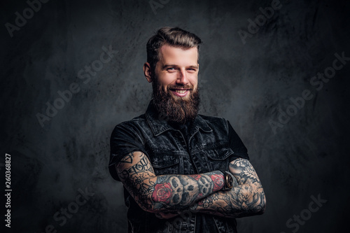 Portrait of a stylish bearded guy with tattooed hands. Studio photo against dark wall photo