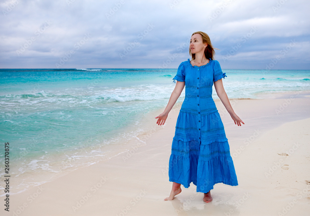 The woman in a long blue dress goes on the sea coast Cayo Largo island, Cuba The woman in a long blue dress goes on the sea coast Cayo Largo island, Cuba