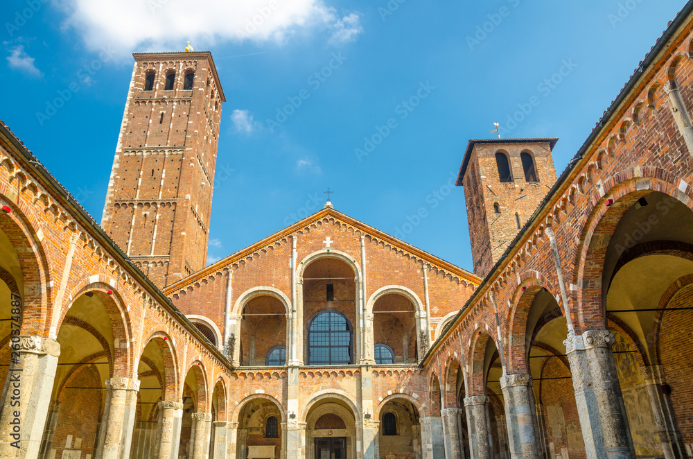 Basilica of Sant'Ambrogio church brick building with bell towers, courtyard, arches, blue sky background, Milan, Lombardy, Italy
