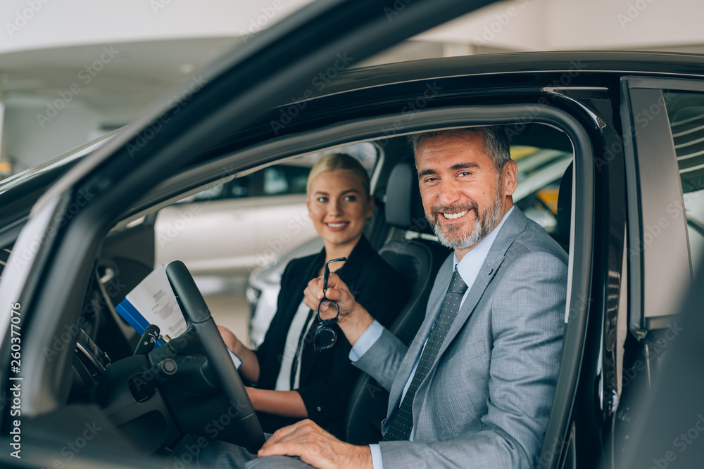 Saleswoman at the dealership showroom talking with customer and helping him to choose a new car