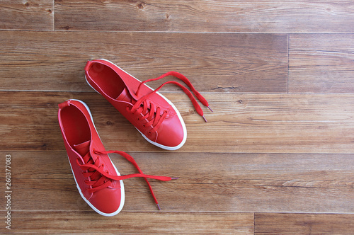 Red sneakers stand on a brown wooden floor. View from above.