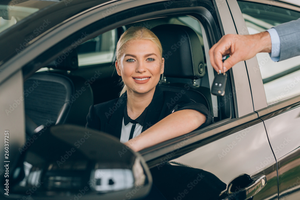 woman sitting in new car while salesman holding car keys beside her in car dealership showroom woman sitting in new car while salesman holding car keys beside her in car dealership showroom