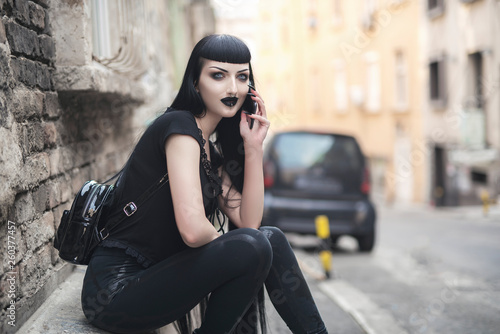 Urban goth girl talking over her cell phone, sitting in an urban outdoor area