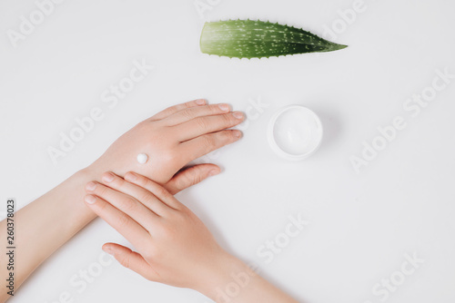 Close up images of female hands applying organic cream, aloe vera leaf and cream container on white background. Flat lay, top view, copy space, minimal style. Beauty concept