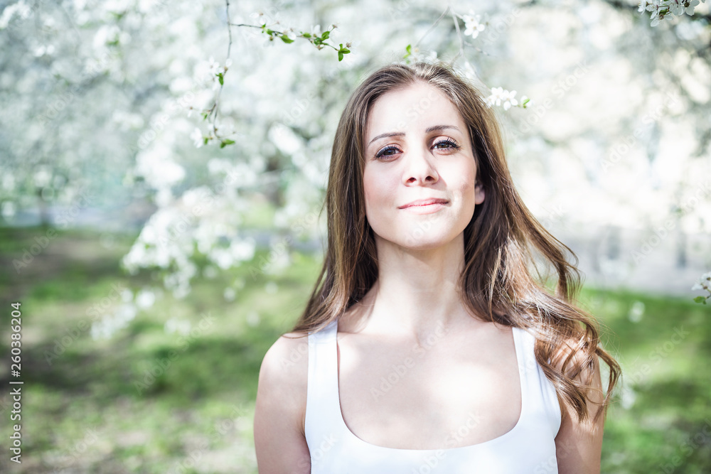 Cheerful long hair young woman in a white t-shirt under the blooming trees. Cheerful long hair young woman in a white t-shirt under the blooming trees.
