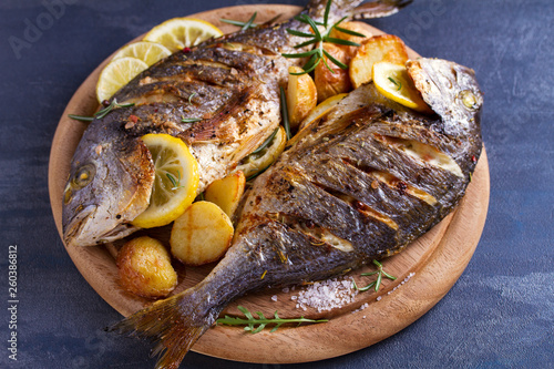 Grilled fish with roasted potatoes, lemon and rosemary on wooden tray