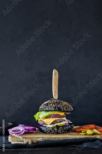 Juicy cheeseburger on a wooden chopping Board. Side view, black background, space for text.