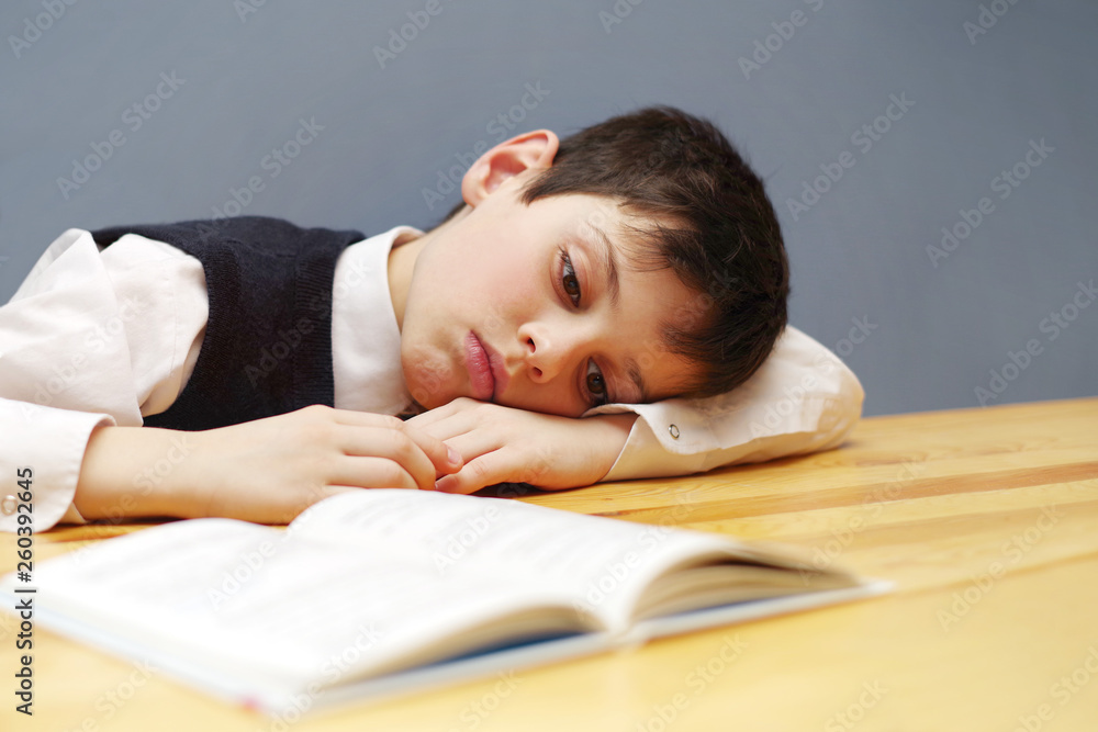 Tired boy, the school student with the book at a table, toned Tired boy, the school student with the book at a table, toned
