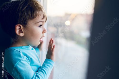 Foto Little boy at home looking trough the window waiting for his mother parents to c