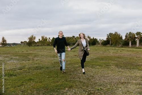 Young Couple in Love Running in a Big Open Outdoor Field in the Spring Holding Hands and Laughing