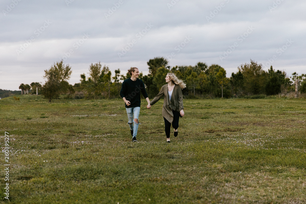 Young Couple in Love Running in a Big Open Outdoor Field in the Spring Holding Hands and Laughing Young Couple in Love Running in a Big Open Outdoor Field in the Spring Holding Hands and Laughing