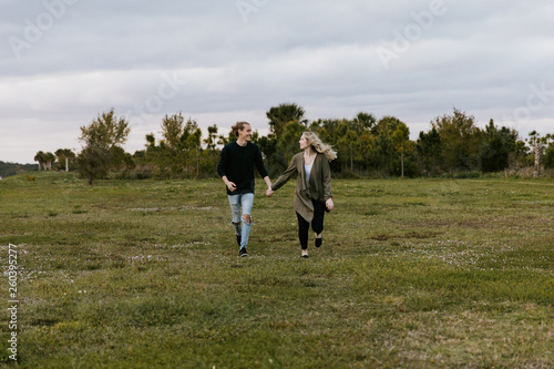Young Couple in Love Running in a Big Open Outdoor Field in the Spring Holding Hands and Laughing © MeganMahoneyPhotos