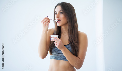Diet. Beautiful young woman eating yogurt in the kitchen at home