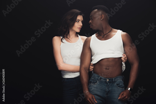 beautiful seductive woman undressing african american man isolated on black