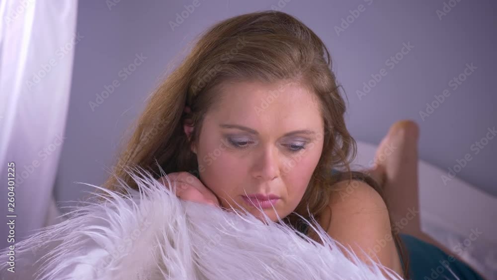 Closeup shoot of plump sexy pretty caucasian female with big breasts looking at camera while lying on the bed posing with soft fur cover indoors Closeup shoot of plump sexy pretty caucasian female with big breasts looking at camera while lying on the bed posing with soft fur cover indoors