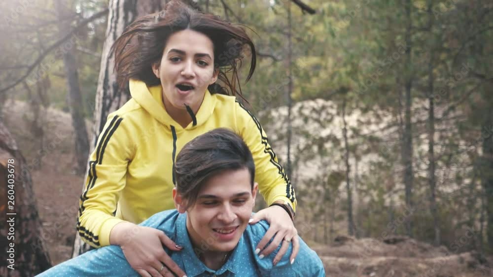 Happy brunette girl sitting on the back of her Mr.Right in a pine forest in slo-mo Happy brunette girl sitting on the back of her Mr.Right in a pine forest in slo-mo