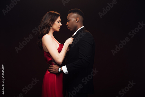 beautiful woman in red dress posing with african american man in suit isolated on black with copy space
